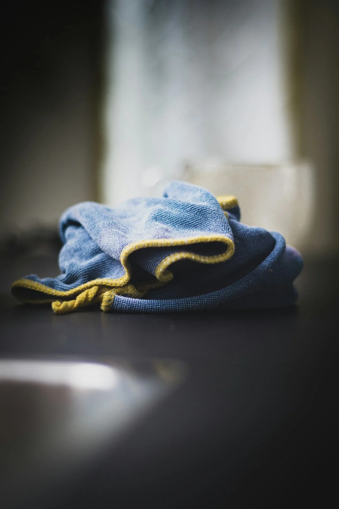 Anonymous male wearing yellow latex gloves and dark t shirt wiping mirror in bathroom with paper napkin