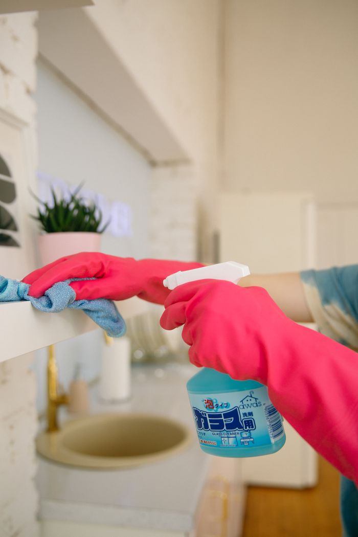Person using spray bottle and cloth to clean a kitchen shelf, helping keep the space hygienic and spotless.